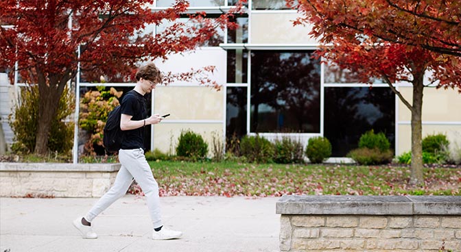 Male student walking with Mohler hall in background.