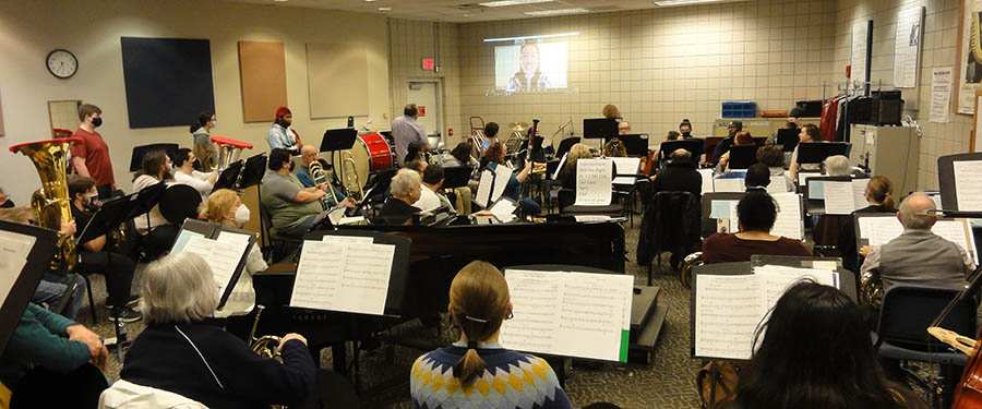 A picture of the Columbus State Concert Band performing for composer Carrie Magin. She is seen projected on the wall from her location in New York.